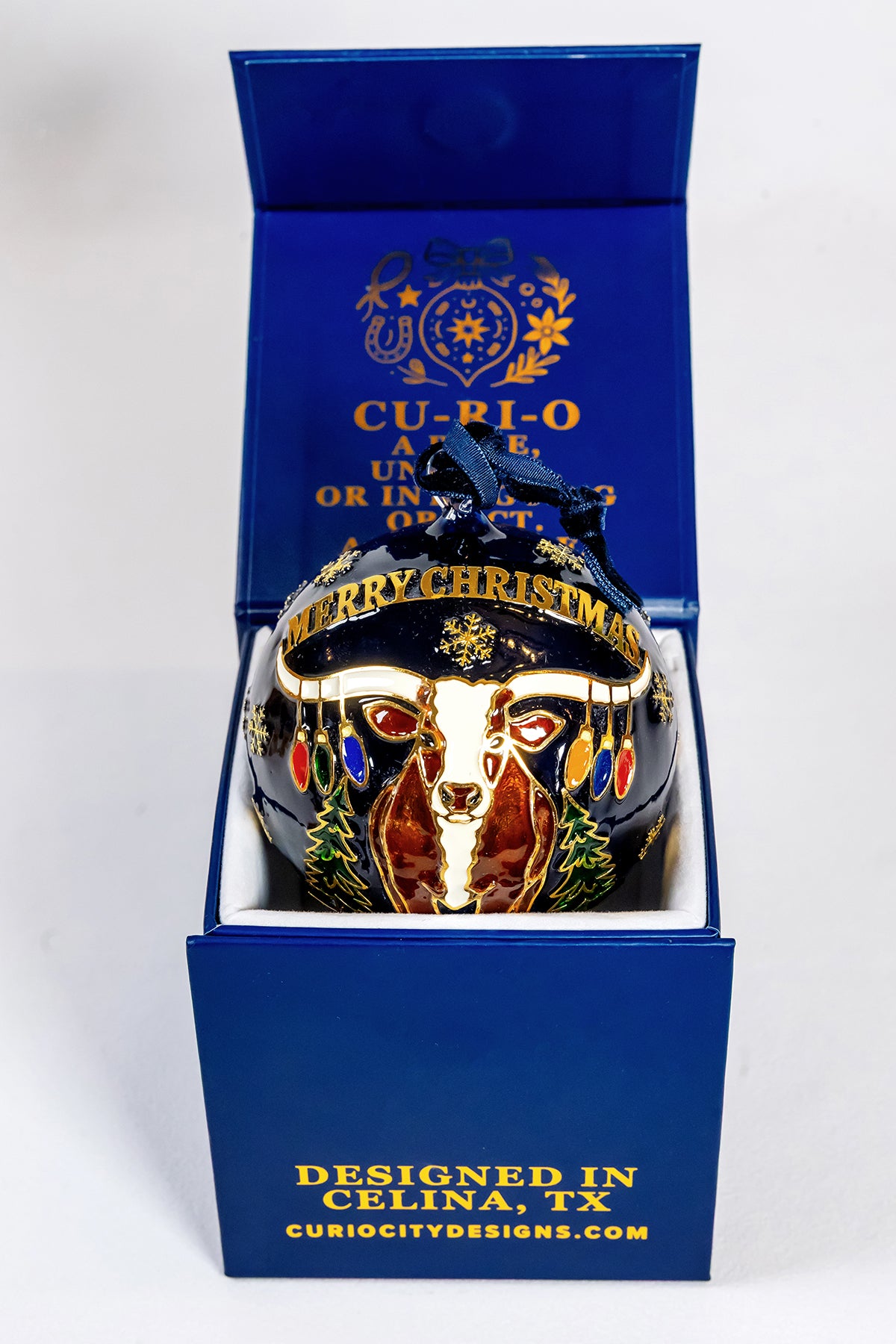 Celina longhorn Christmas scene on the reverse of the hand-painted glass ornament, presented in its blue CurioCity Designs gift box.