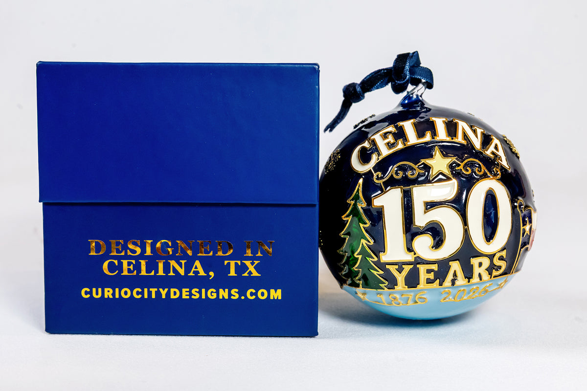Celina 150 Years anniversary glass ornament beside the blue CurioCity Designs gift box marked Designed in Celina, TX.