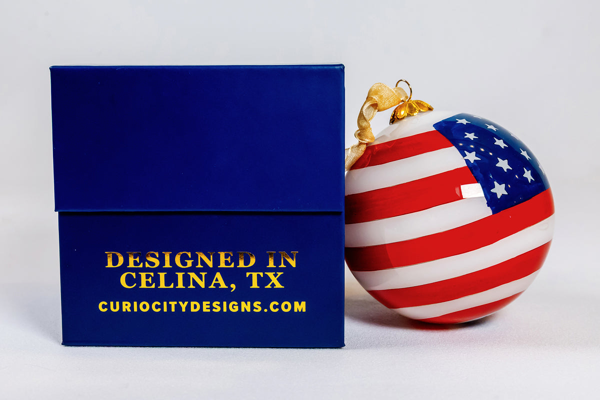 Reverse view of the God Bless the USA 250 Years hand-painted glass ornament beside its navy gift box.