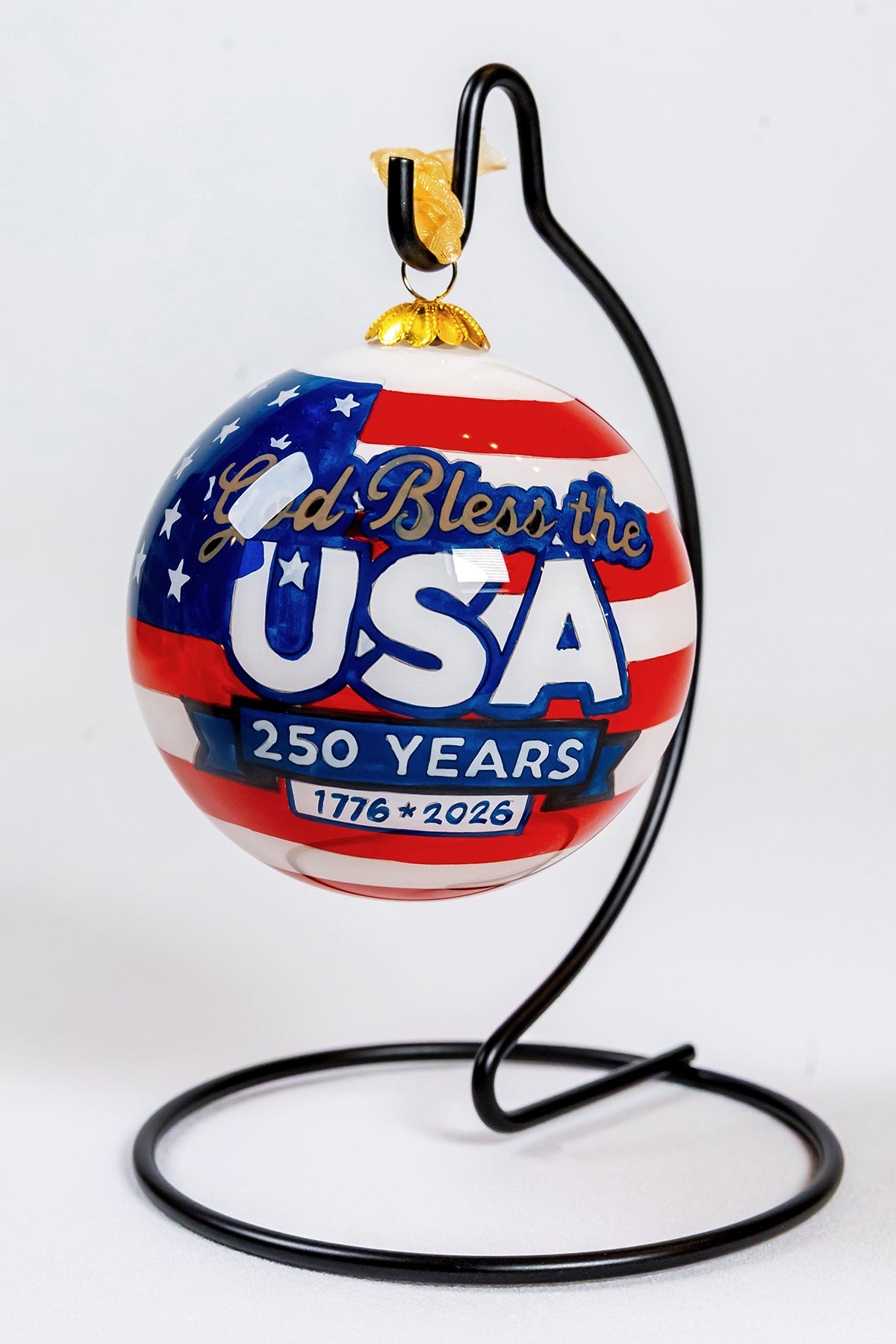 Front view of the God Bless the USA 250 Years glass ornament hanging from a black ornament stand.