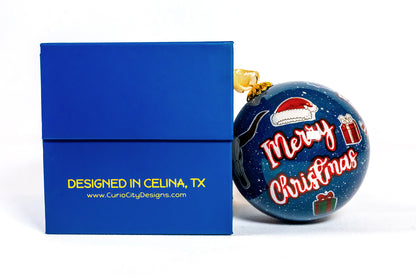 Prosper Texas hand-painted glass ornament with candy cane beside CurioCity Designs blue gift box