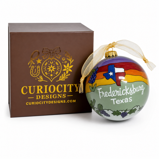 Close-up of a reverse hand-painted Fredericksburg Texas glass Christmas ornament with Texas flag, bluebonnet, and grapevine artwork