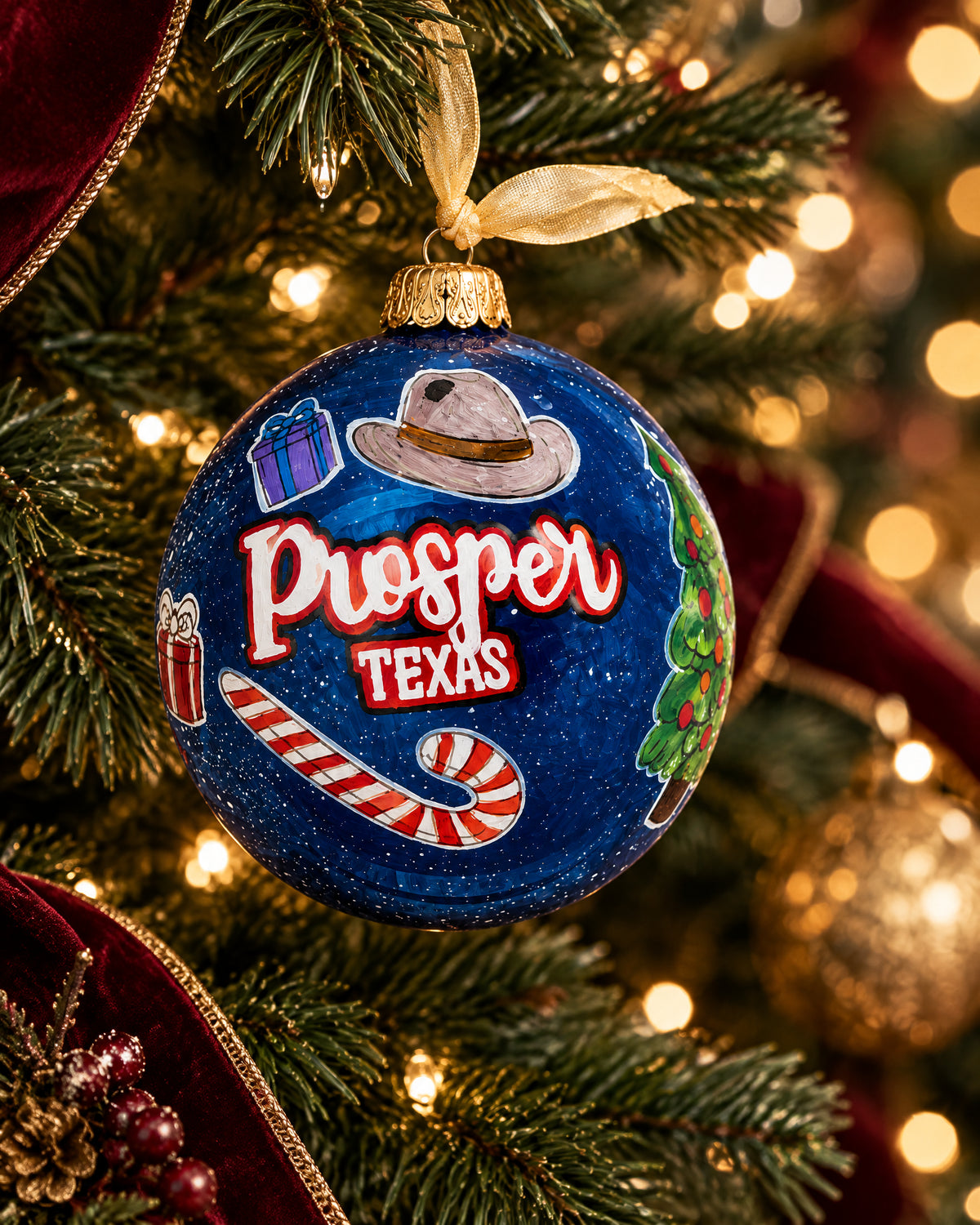 A Prosper Christmas hand-painted glass ornament hanging on a Christmas tree