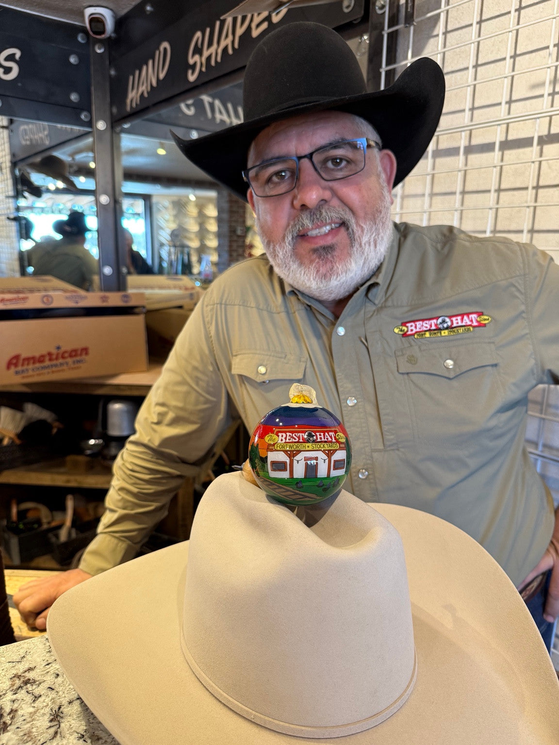 A client holding The Best Hat Store custom glass ornament on a cream cowboy hat.