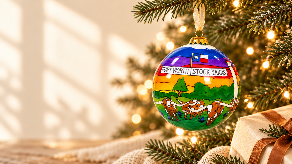 Original Fort Worth Stockyards glass ornament with colorful cattle-drive artwork hanging on a warmly lit Christmas tree.