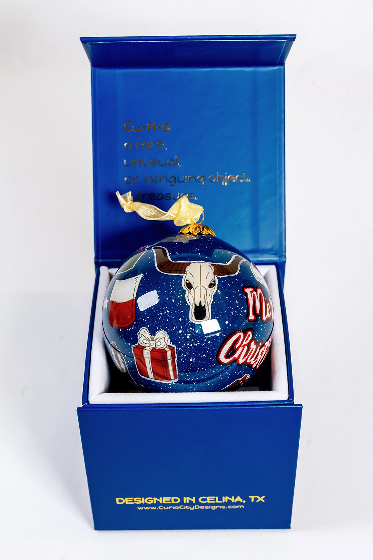 Close view of Merry Christmas Prosper Texas ornament beside CurioCity Designs blue gift box