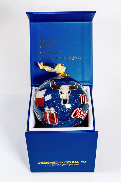 Close view of Merry Christmas Prosper Texas ornament beside CurioCity Designs blue gift box