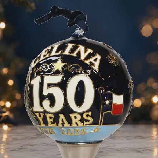 Rotating Celina 150th Anniversary hand-painted glass ornament with anniversary lettering and longhorn artwork against a luxury Christmas background.